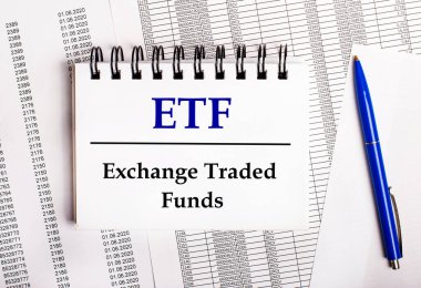 Masada mavi bir kalem ve üzerinde ETF Ticaret Fonları yazan bir defter bulunan tablolar ve raporlar bulunuyor.