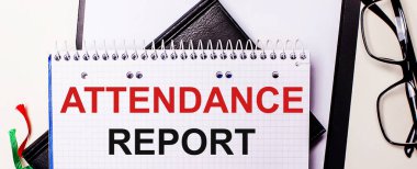 ATTENDANCE REPORT kelimeleri siyah çerçeveli gözlüklerin yanındaki beyaz bir deftere kırmızı ile yazılmıştır.