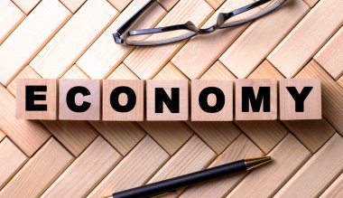 ECONOmy kelimesi tahta bir arka planda, bir kalem ve gözlüğün yanındaki tahta küplere yazılmıştır..