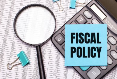 On the table are reports, a magnifying glass, a calculator, and a blue note sticker with the words FISCAL POLICY. Business concept clipart