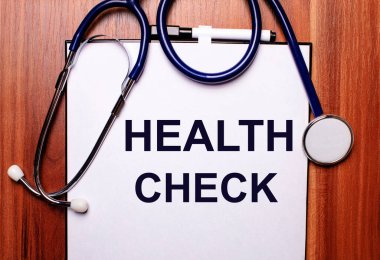 Ahşap bir arka planda steteskop ve üzerinde sağlık kontrolü yazan bir kağıt parçası bulunur. Düz yatıyordu. Tıbbi konsept