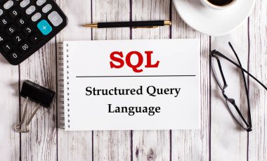 SQL Yapılandırılmış Sorgu Dili, bir hesap makinesi, kahve, bardak ve bir kalem yakınında beyaz bir not defterine yazılmıştır. İş konsepti