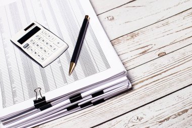 Beyaz bir hesap makinesi ve bir kalem beyaz tahta bir masanın üzerinde duruyor. İş konsepti