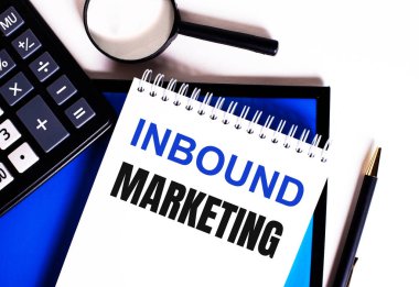 Mavi bir arkaplanda, hesap makinesinin yanında, büyüteç ve kalem, INBOUND MARKETING yazılı bir defter