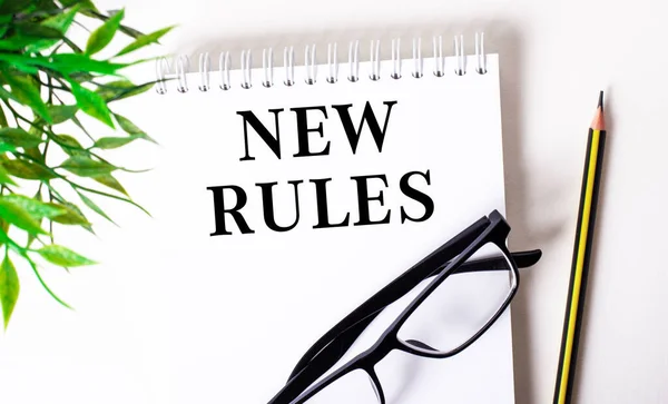 NEW RULES is written in a white notebook next to a pencil, black-framed glasses and a green plant.