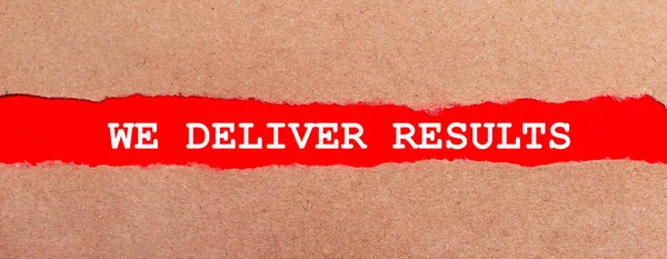 A strip of red paper under the torn brown paper. White lettering on red paper WE DELIVER RESULTS. View from above