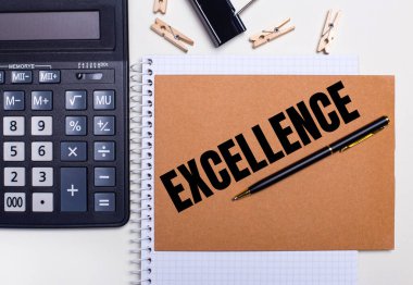 Masaüstünde bir hesap makinesi, bir dizüstü bilgisayarın yanında EXCELLENCE yazılı bir kalem ve mandallar var. İş konsepti. Yukarıdan görüntüle