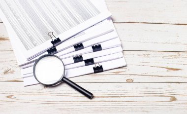 Bir büyüteç ve bir yığın belge açık ahşap bir masanın üzerinde duruyor. İş konsepti. Boşluğu kopyala