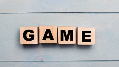 Açık mavi ahşap zemin üzerinde oyun metni olan tahta küpler.