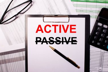 ACTIVE kelimesi beyaz bir kağıda yazılır, gözlük ve hesap makinesinin yanında..