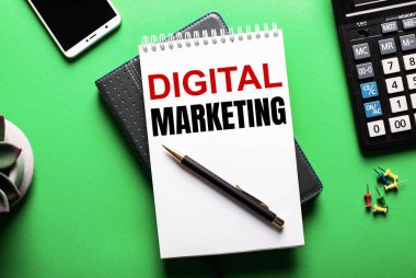 Yeşil bir arkaplanda - bir telefon, bir hesap makinesi ve DiGITAL MARKETING yazılı bir günlük