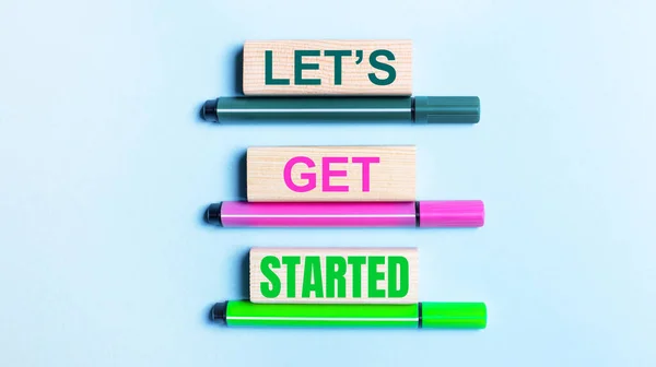 ライトブルーの背景には 3つの多色のフェルトチップペンと木製のブロックがあり Let Get Startedテキスト — ストック写真