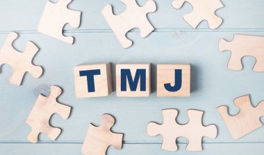 Boş bulmacalar ve üzerinde TMJ yazılı tahta küpler açık mavi bir arkaplanda yatıyor..