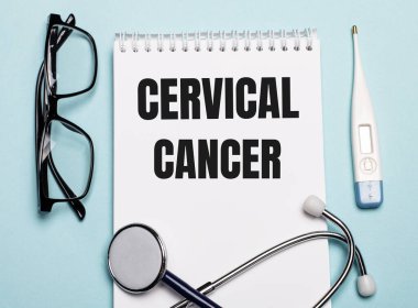 Stetoskop, gözlük ve açık mavi arka planda elektronik termometrenin yanında beyaz bir not defterine yazılmış. Tıbbi konsept.