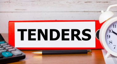 Kağıtlar için kırmızı klasör TENDERS metni, beyaz alarm saati, hesap makinesi ve kalem masaüstünde. İş konsepti