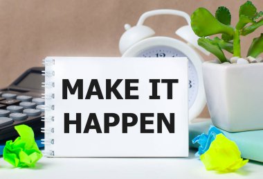 Bir saksıda çiçek, hesap makinesi, beyaz alarmlı saat, çok renkli kağıt parçaları ve masaüstünde 