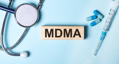Mavi bir arka planda, steteskop, şırınga ve haplar ve üzerinde MDMA yazan tahta bir blok. Tıbbi konsept