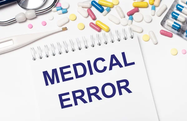 On a light background, multi-colored pills, a stethoscope, an electronic thermometer and a notebook with the text MEDICAL ERROR. Medical concept.