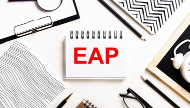 Bir ışık masasında defterler, bir büyüteç, bir çalar saat, bir gözlük ve bir kalem vardır. Ve ortada EAP Personel Yardım Programı metninin olduğu bir defter var.