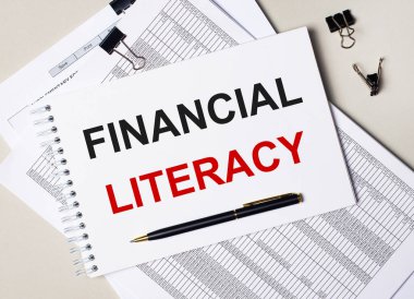 Masaüstünde belgeler, kalem, siyah ataçlar ve içinde FINANCIAL LITERACY metni olan bir defter var. İş konsepti