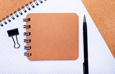 Ahşap bir arka planda, bir defter, siyah bir kalem, bir ataç ve içine metin eklenecek kahverengi bir defter. Şablon. İş konsepti