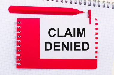 Beyaz bir not defterinde, kırmızı bir kalem, kırmızı bir not defteri ve üzerinde CLAIM DENIED yazan beyaz bir sayfa.