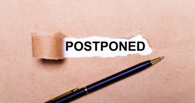 Yırtık bir Kraft kâğıdı, beyaz arkaplan ve metin POSTPONED. Yakınlarda siyah bir kol var. Yukarıdan görüntüle