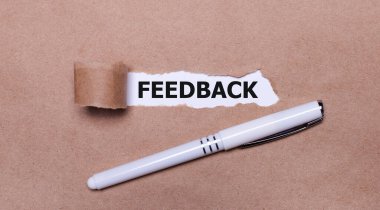 Kraft kağıdında, beyaz bir kalem ve üzerinde FEEDback yazan beyaz bir kağıt şeridi..