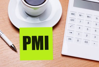 Ahşap masada beyaz bir fincan kahve, bir kalem, beyaz bir hesap makinesi ve PMI Proje Yönetim Enstitüsü yazılı yeşil bir çıkartma vardır. İş konsepti