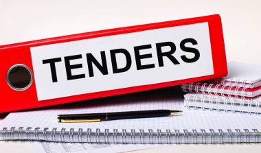 Masaüstünde not defterleri, bir kalem ve içinde TENDERS metni olan kağıtlar için kırmızı bir klasör var. İş konsepti