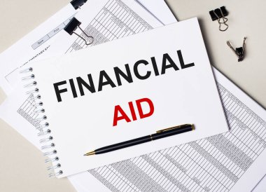 Masaüstünde belgeler, kalem, siyah ataç ve FINANCIAL AID yazılı bir defter var. İş konsepti