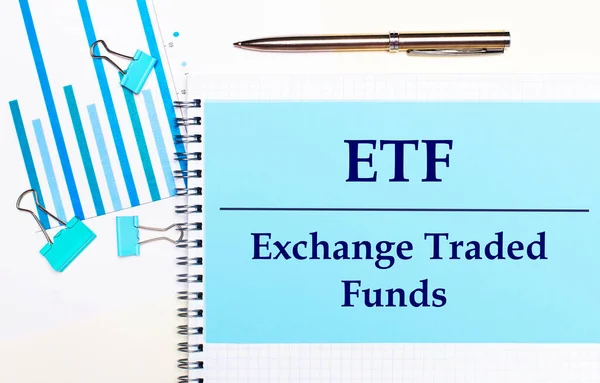 On a light background - light blue diagrams, paper clips and a sheet of paper with the text ETF Exchange Traded Funds. View from above. Business concept