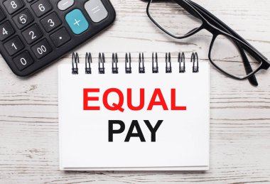 Açık tahta bir hesap makinesinde, gözlükler ve içinde EQUAL Pay yazan boş bir not defteri. İş konsepti