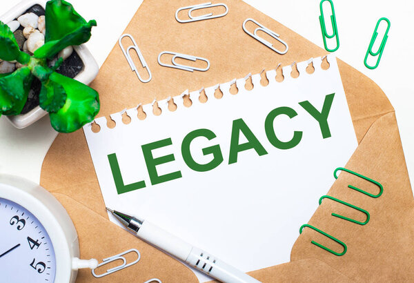На светлом фоне - открытый конверт, белый будильник, зеленое растение, белые и зеленые скрепки, белая ручка и лист бумаги с текстом LEGACY