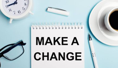 Açık mavi arka planda, kahveli beyaz bir kupa, beyaz bir çalar saat, beyaz bir kalem ve üzerinde 