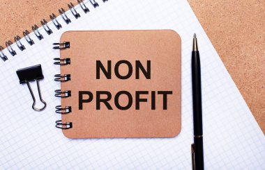 Tahta arka plan not defteri, siyah kalem, ataç ve NON PROFIT yazılı kahverengi not defteri. İş konsepti