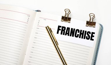 Hafif bir arka planda, açık bir defter, altın ataçlı bir kağıt ve FRANCHISE yazısı ve altın bir kalem. Yukarıdan bak. İş konsepti