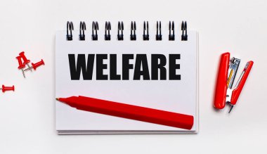 Hafif bir arka planda, kırmızı bir kalem, kırmızı bir zımba, kırmızı ataç ve WELFARE yazılı bir defter.