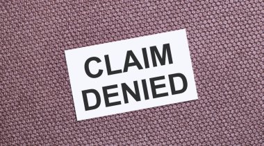 Kahverengi arkaplanda, üzerinde CLAIM DENIED yazılı beyaz dikdörtgen bir kart
