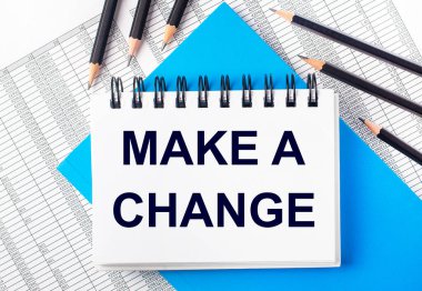 Üzerinde metin olan beyaz defter mavi arka planda siyah kalemlerin yanında bir değişiklik yapıyor ve raporlar yazıyor. İş konsepti