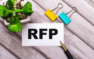 Ahşap bir arka planda, RFP yazılı beyaz bir kart, sarı ve yeşil ataçlar ve saksıda bir bitki. Yukarıdan görüntüle
