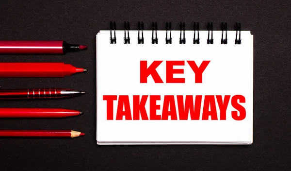 KEY TAKEAWAYS yazılı beyaz bir not defteri, kırmızı kalemlerin, kalemlerin ve siyah arkaplandaki işaretlerin yanında beyaz bir not defteri..