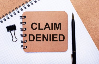 Tahta arka plan not defteri, siyah kalem, ataç ve CLAIM DENIED yazılı kahverengi not defteri. İş konsepti