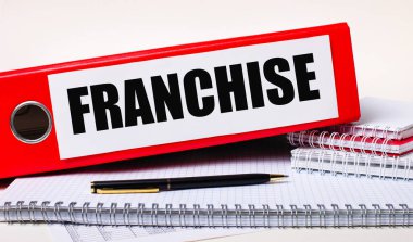 Masaüstünde FRANCHISE yazılı kağıtlar için not defterleri, bir kalem ve kırmızı klasör var. İş konsepti