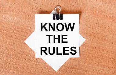 Siyah bir ataçın altındaki ahşap bir masanın üzerinde beyaz bir sayfa uzanıyor.