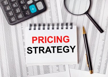 Masada raporlar, bir büyüteç, bir hesap makinesi, bir kalem ve üzerinde STRATEGY yazan beyaz bir defter var. İş konsepti