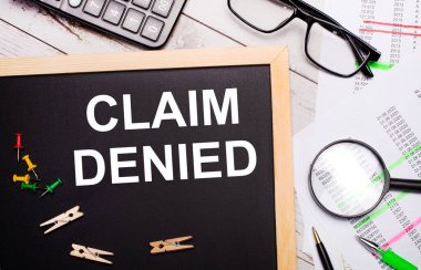 Masaüstünde bir hesap makinesi, raporlar, gözlükler, bir büyüteç, kalemler ve mandallı bir pano ve CLAIM DENIED mesajı var. İş konsepti.