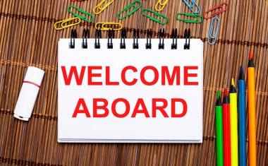 Ahşap bir masada, çok renkli kalemler, ataçlar, beyaz bir flaş bellek ve 