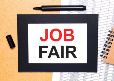 Ahşap bir masanın üzerinde siyah açık bir kalem, kahverengi bir not defteri ve siyah çerçeveli bir kağıt parçası var. Yukarıdan görüntüle.