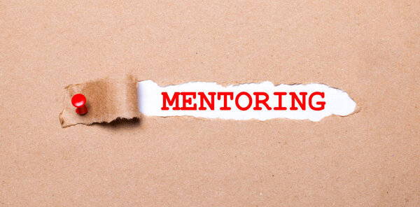 Beneath the torn strip of kraft paper attached with a red button is a white paper MENTORING